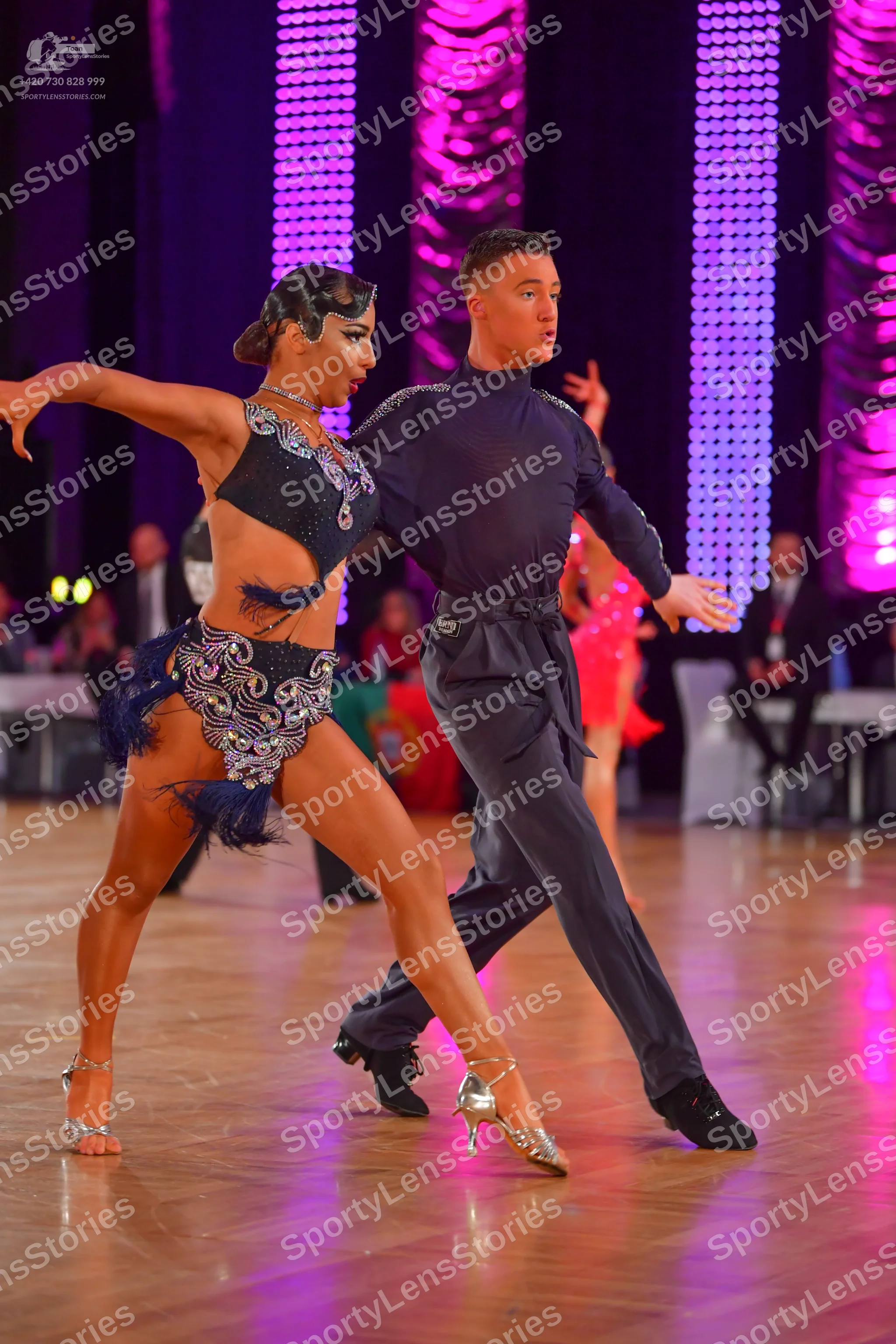 Dancesport competitor: Female dancer: dark navy or black latin dance costume heavily embellished with s