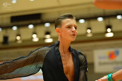 Dancesport competitor: Male dancer: black top with black mesh/fishnet sleeves and a cross necklace