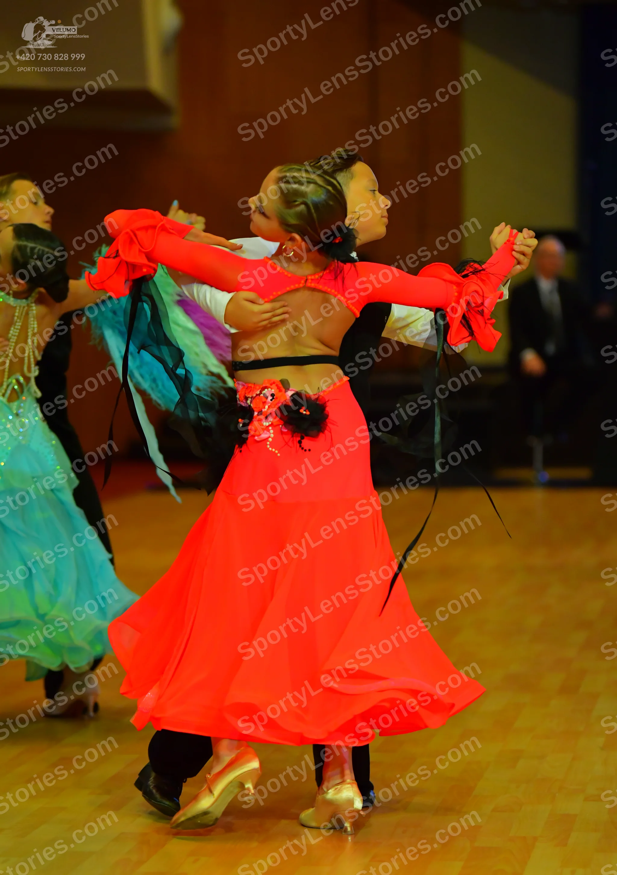 Dancesport competitor: Female dancer in foreground: red latin dress with long ruffled sleeves, an open