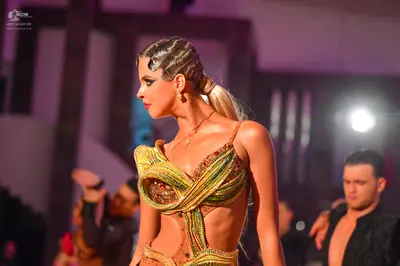 Dancesport competitor: Female dancer: gold and green Latin dance dress with sequins and cutouts