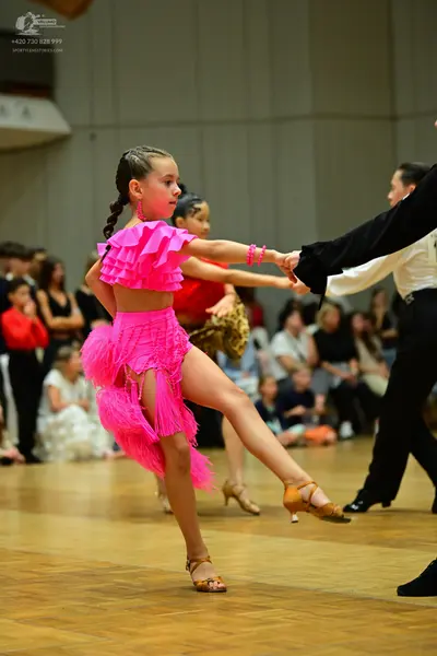 Dancesport competitor: Female dancer: bright pink latin dance costume featuring a ruffled top and a lon