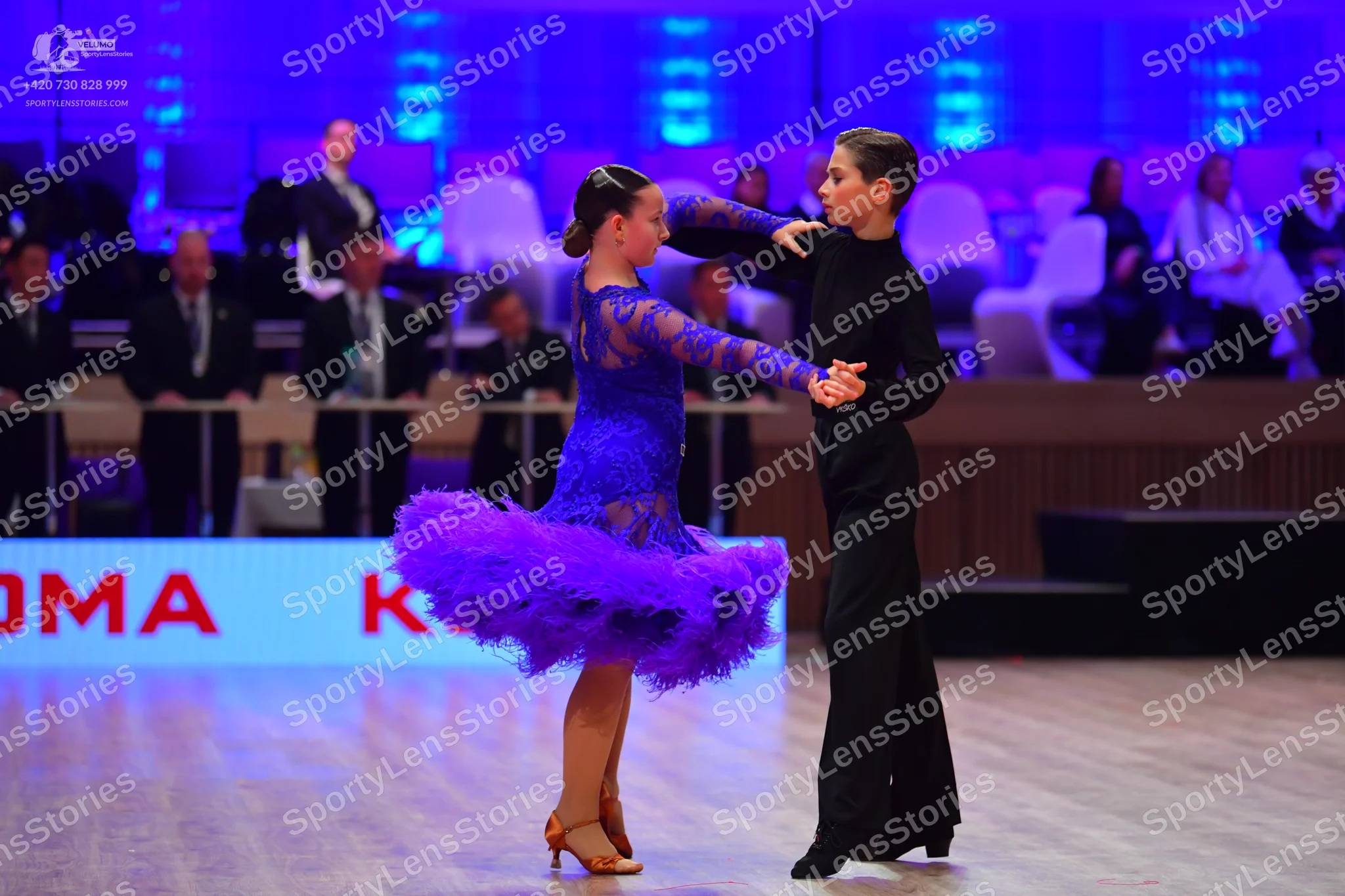 Dancesport competitor: Female dancer: blue/purple Latin dance dress with a lace bodice and long sleeves