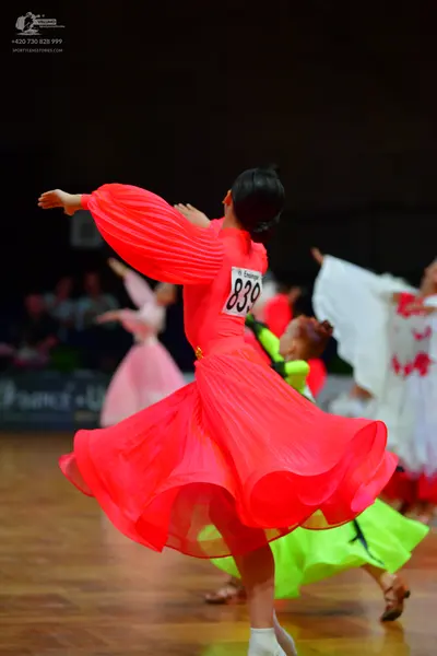 Dancesport competitor: Female dancer in foreground: reddish-pink long-sleeved ballroom dress with pleat