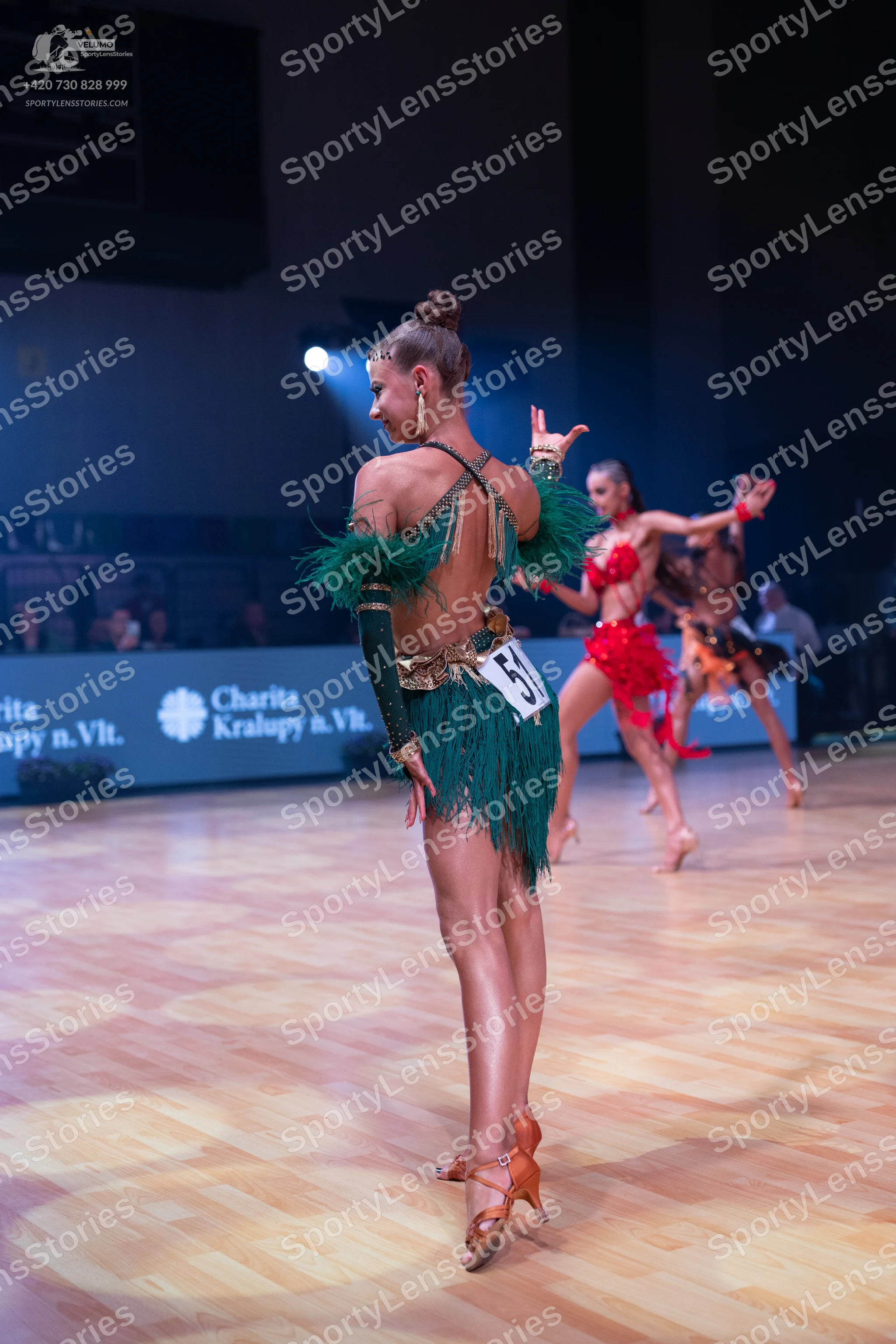 Dancesport competitor: Female dancer in foreground: green latin dress with long fringe and matching lon