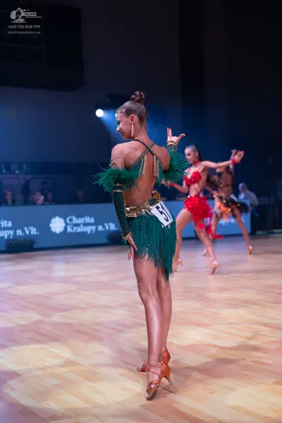 Dancesport competitor: Female dancer in foreground: green latin dress with long fringe and matching lon