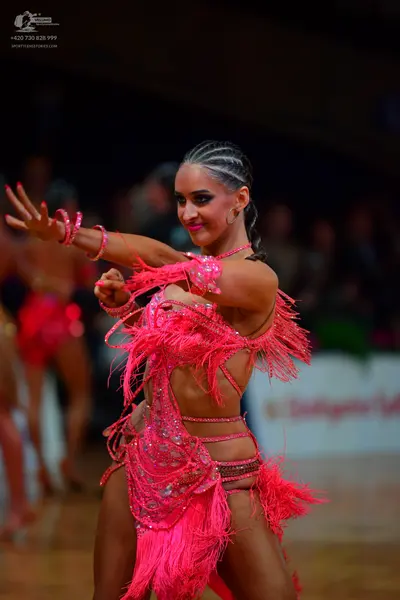 Dancesport competitor: Female dancer (foreground): bright pink Latin dance dress featuring long fringe,