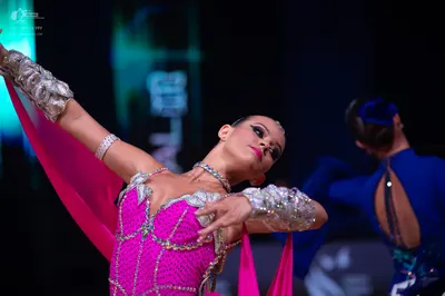 Dancesport competitor: Female dancer in foreground: bright pink Latin dance dress with silver and white