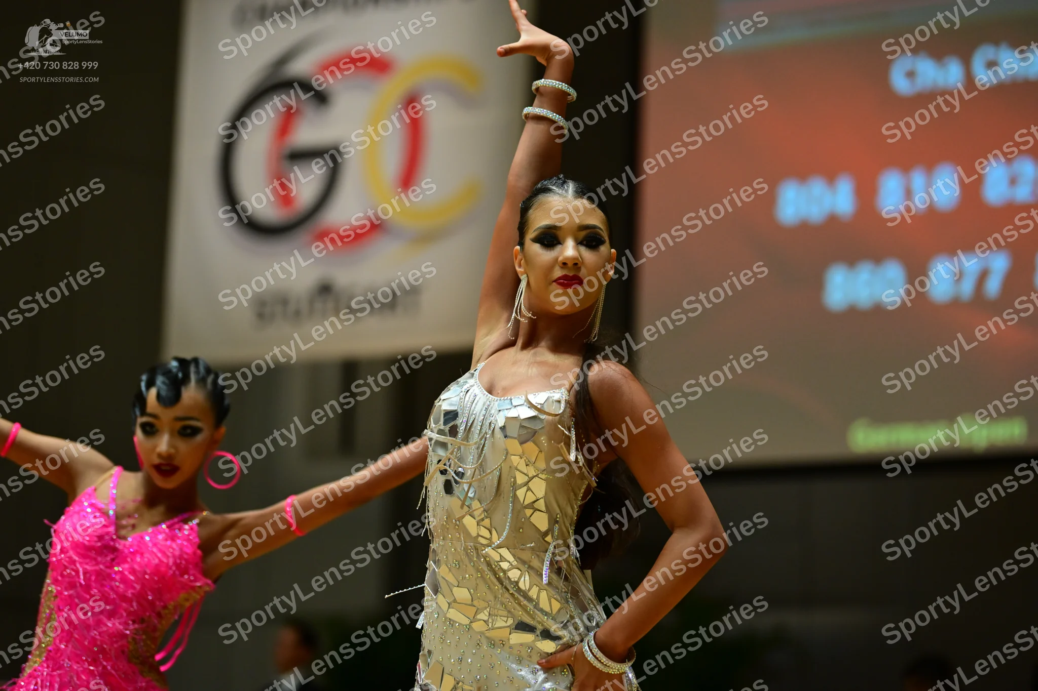 Dancesport competitor: Female dancer on left: bright pink latin dress with sequins and fringe, pink hoo