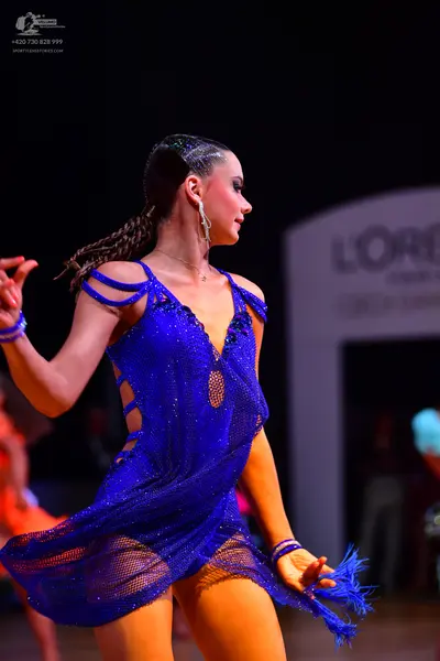 Dancesport competitor: Female dancer: blue Latin dance dress with mesh fabric, cutouts, and fringe at t