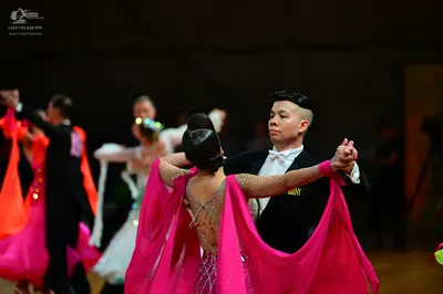Dancesport competitor: Female dancer in foreground: pink latin dress with sheer, flowing sleeves and a 