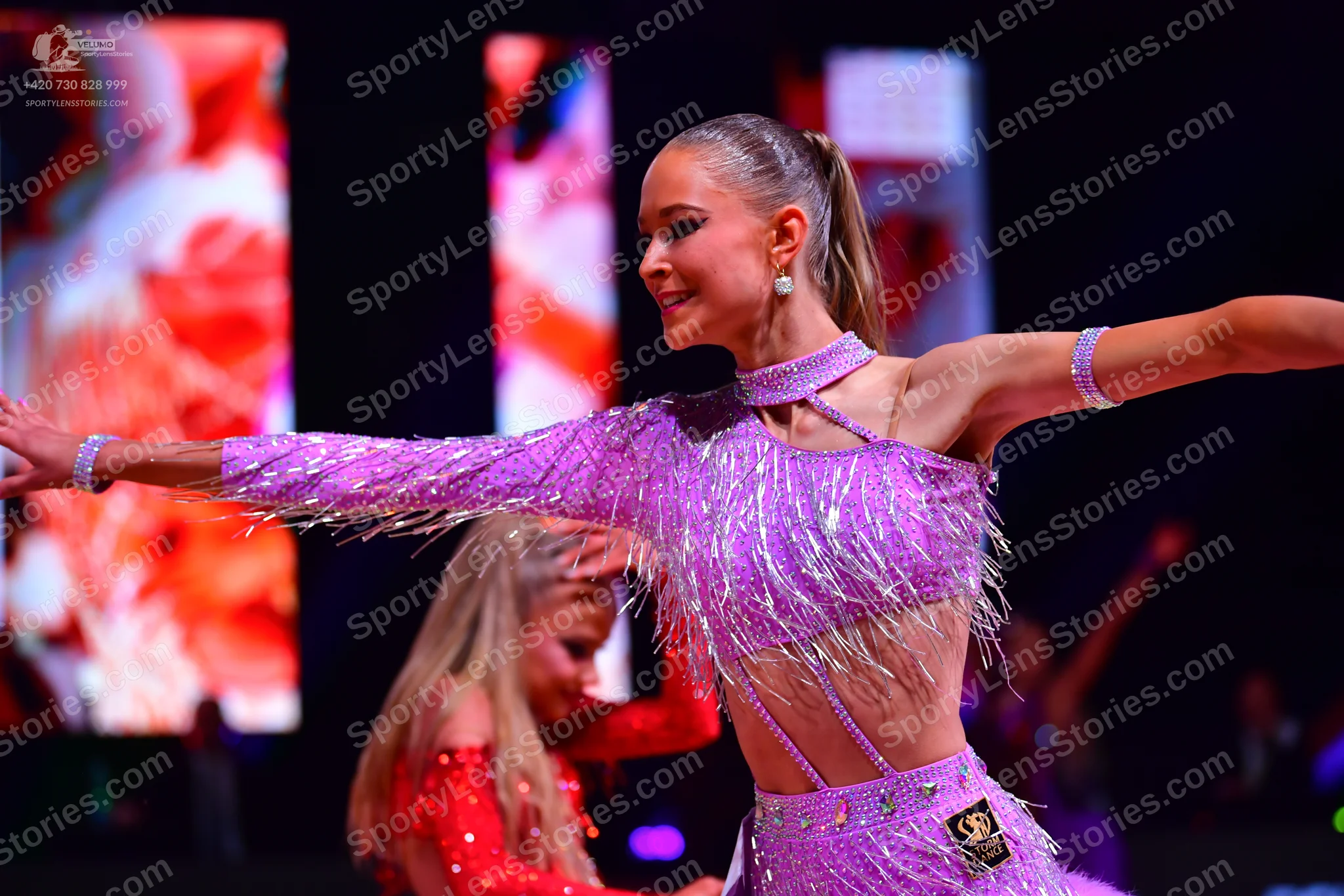 Dancesport competitor: Female dancer in foreground: lavender Latin dance dress with heavy fringe and se