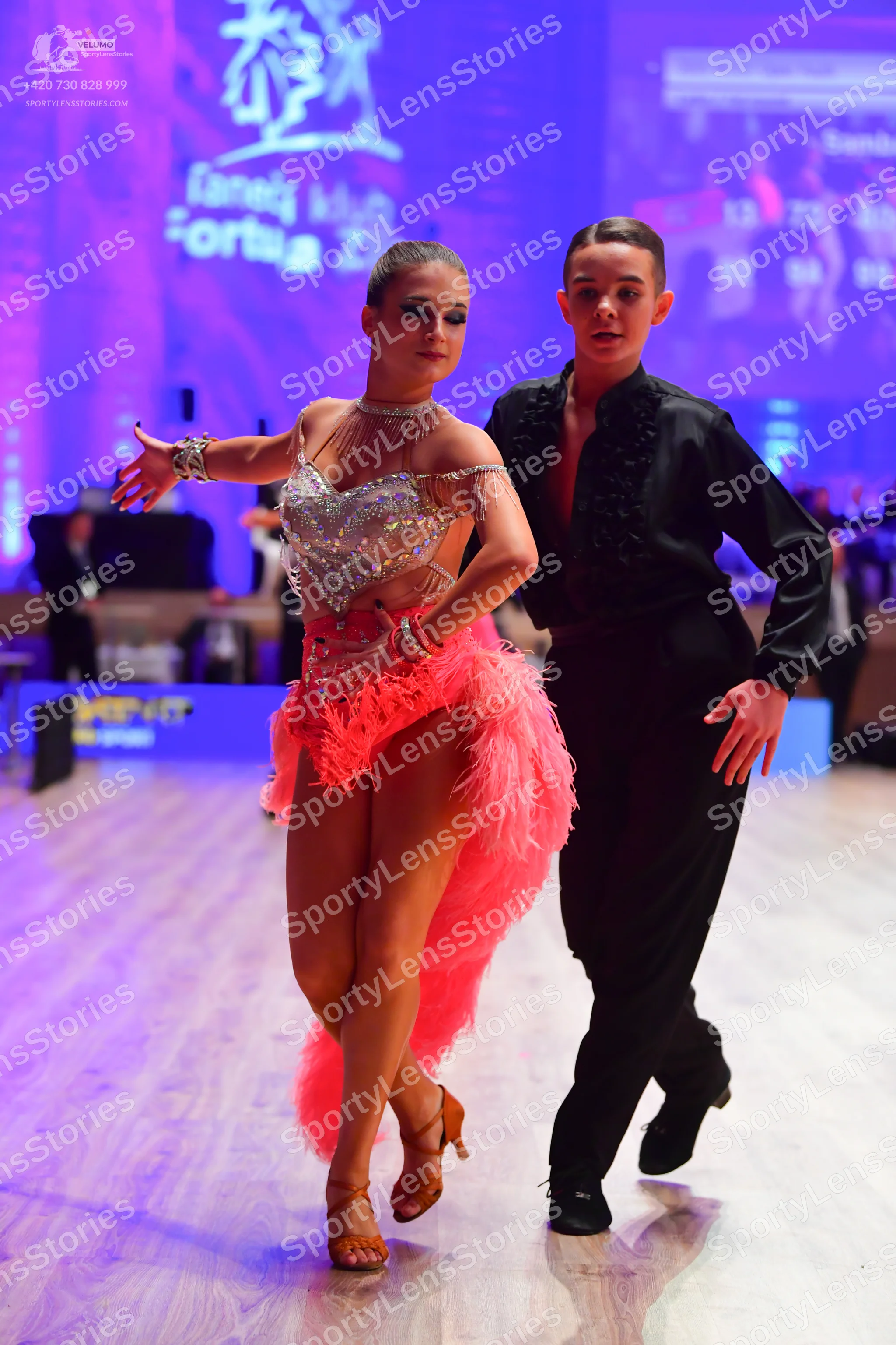 Dancesport competitor: Female dancer: silver sequined Latin bodice with thin straps, bright pink feathe