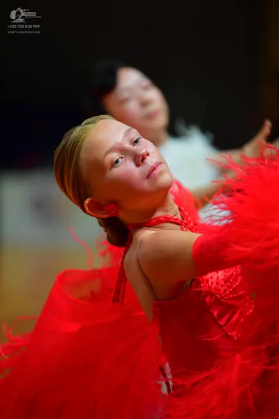 Dancesport competitor: Foreground dancer: red Latin dress with feathers