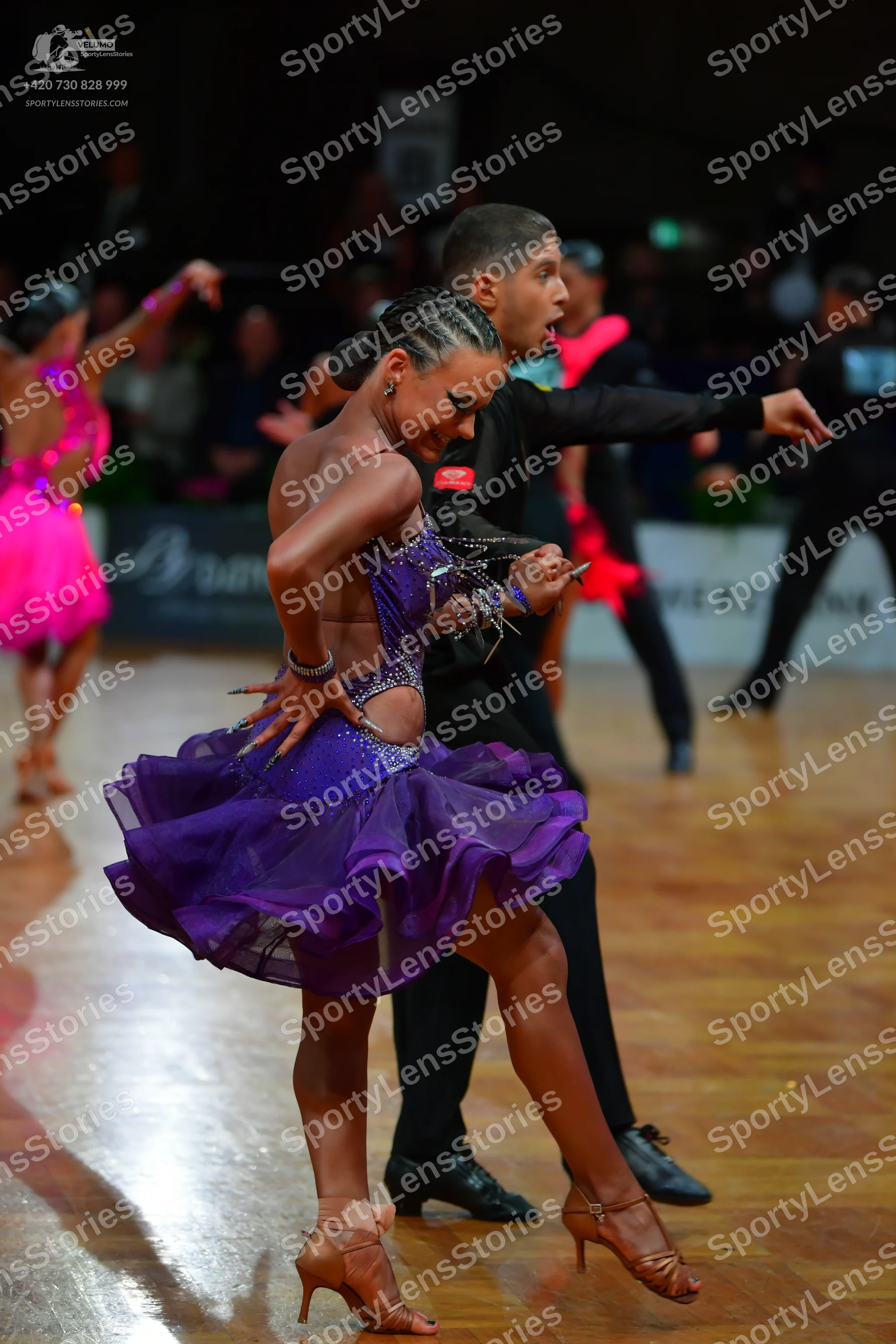 Dancesport competitor: Foreground female dancer: purple latin dress with a sequined bodice and a ruffle