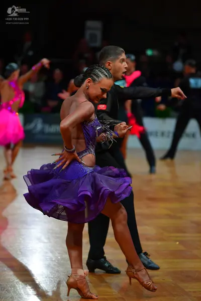 Dancesport competitor: Foreground female dancer: purple latin dress with a sequined bodice and a ruffle