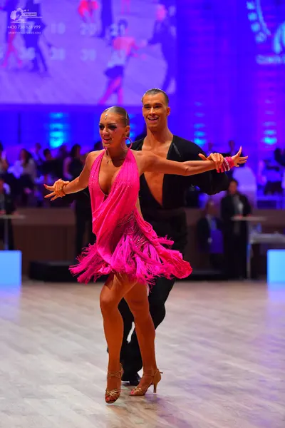Dancesport competitor: Female dancer: bright pink Latin dress with long fringe and a deep V-neckline, w