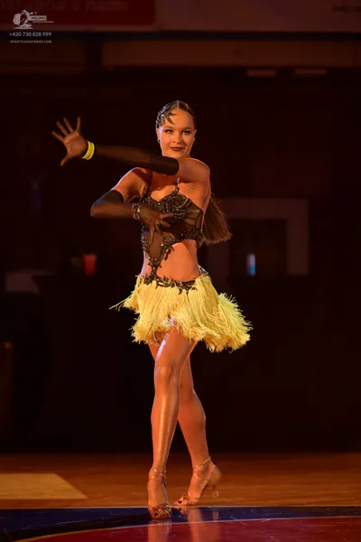 Dancesport competitor: Female dancer: black and gold latin dress with a yellow fringed skirt and long b