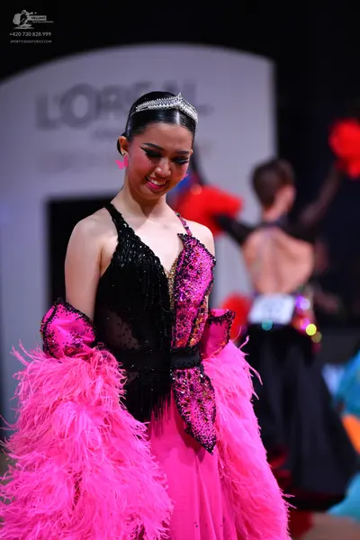 Dancesport competitor: Female dancer (foreground): black and bright pink latin dress with a sequined bl