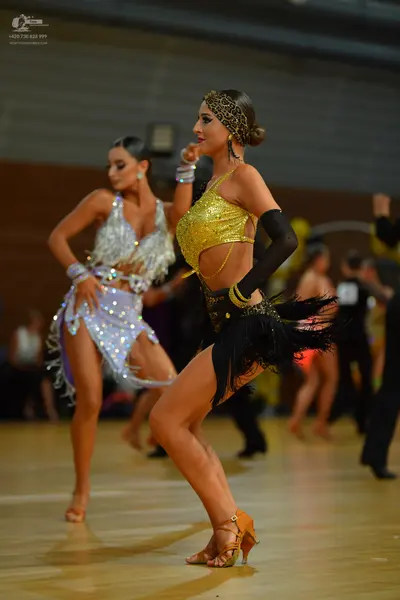 Dancesport competitor: Female dancer in foreground: gold sequined crop top, black skirt with heavy blac