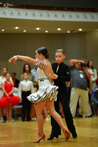 Dancesport competitor: Female dancer: white Latin dress with black trim and a layered, ruffled skirt
