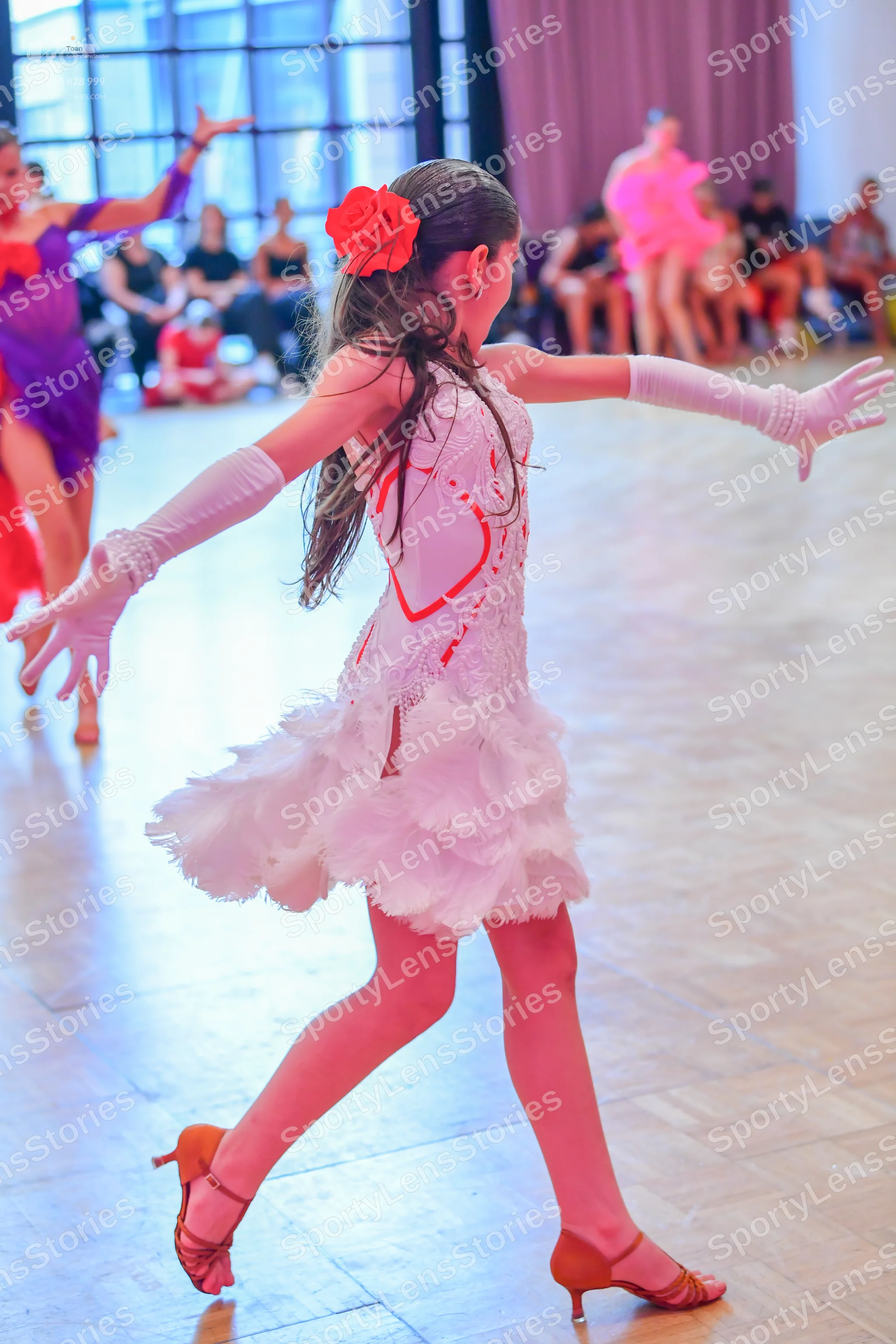 Dancesport competitor: Female dancer in foreground: white Latin dress with red patterns on the bodice a