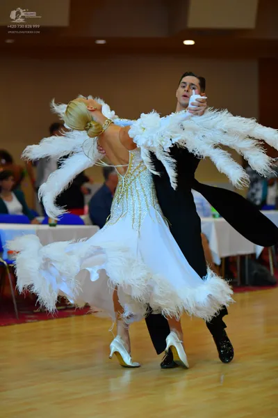 Dancesport competitor: Female dancer: white ballroom dress with gold sequin patterns and large white fe