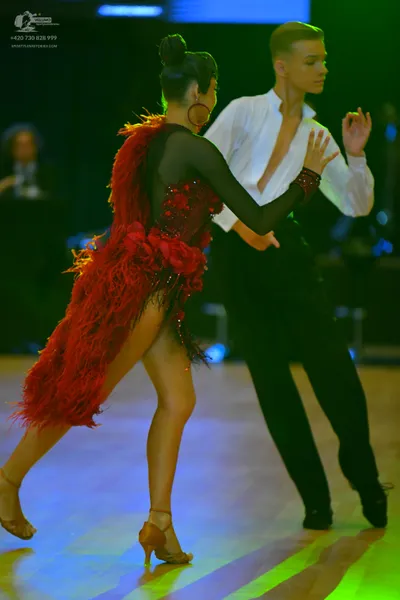 Dancesport competitor: Female dancer: red latin dress with feathers, sequins, and sheer sleeves, and la