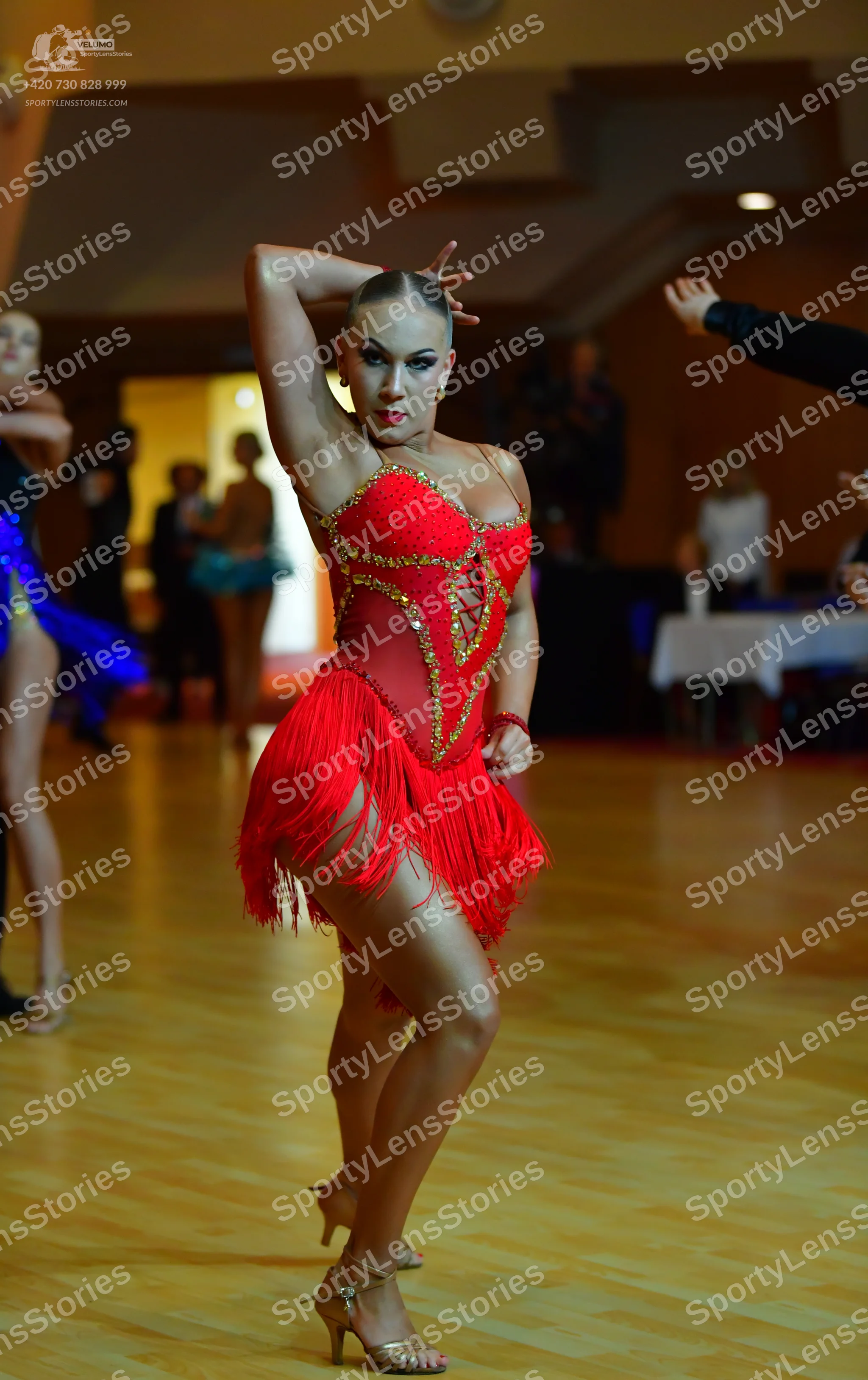 Dancesport competitor: Female dancer in foreground: red latin dress with fringe and gold sequin embelli