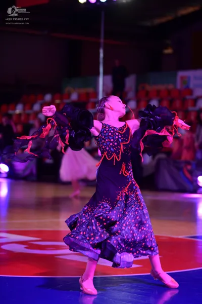 Dancesport competitor: Female dancer: black latin dress with orange patterns and large, ruffled black s