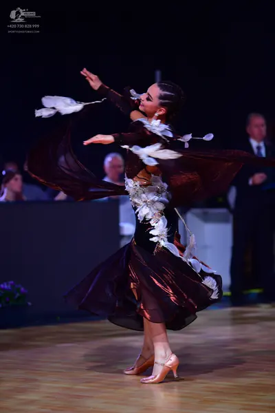 Dancesport competitor: Female dancer: deep burgundy long-sleeved ballroom dress with large white feathe