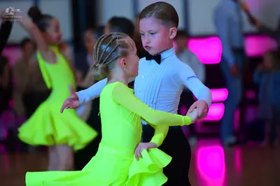 Dancesport competitor: Female dancer in foreground: neon yellow long-sleeved Latin dress