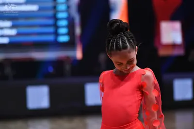 Dancesport competitor: Female dancer: bright red, long-sleeved Latin dress with large, translucent red 