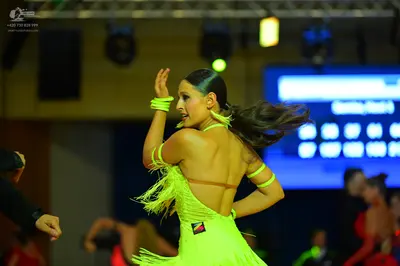Dancesport competitor: Female dancer: lime green Latin dress with fringe and thin straps around arms an