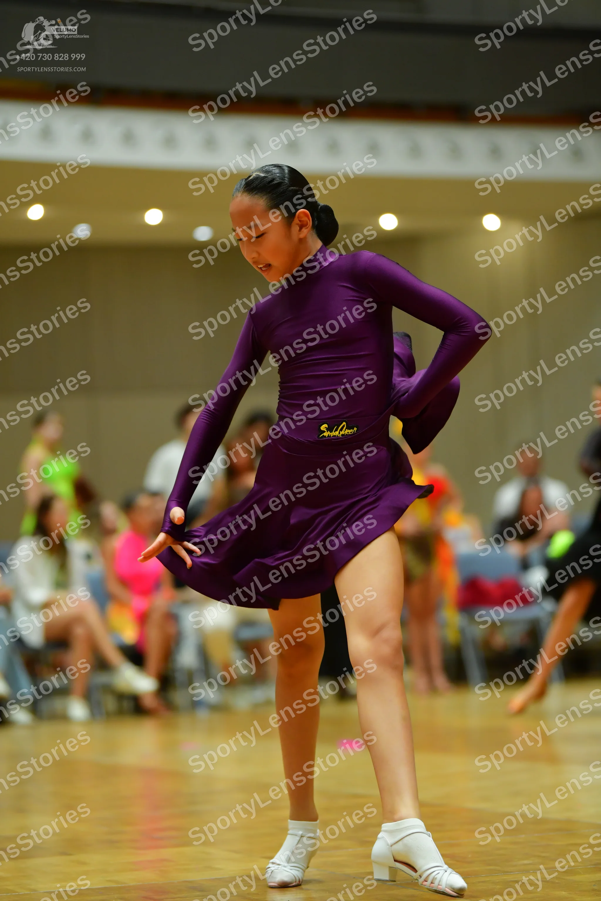 Dancesport competitor: Female dancer in foreground: deep purple, long-sleeved latin dress with a flared
