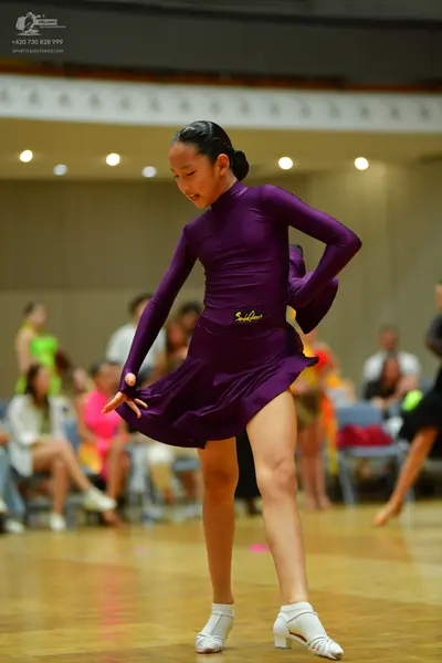 Dancesport competitor: Female dancer in foreground: deep purple, long-sleeved latin dress with a flared