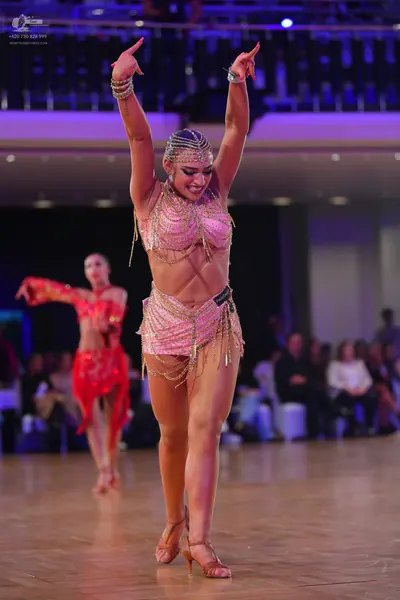 Dancesport competitor: Female dancer in foreground: nude or light pink Latin dance costume with gold be