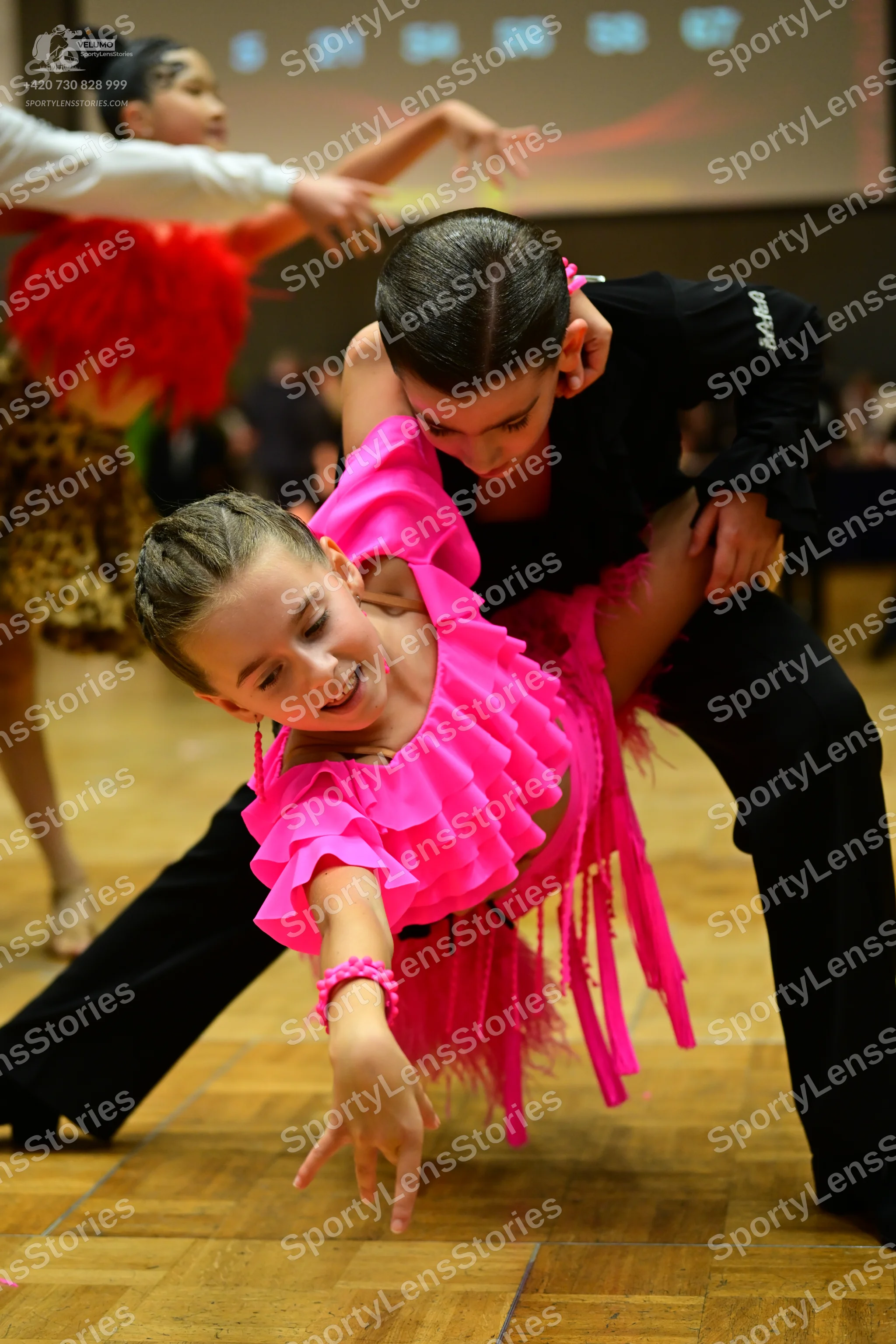 Dancesport competitor #391, #394: Female dancer in foreground: hot pink latin dress with ruffled sleeves and long