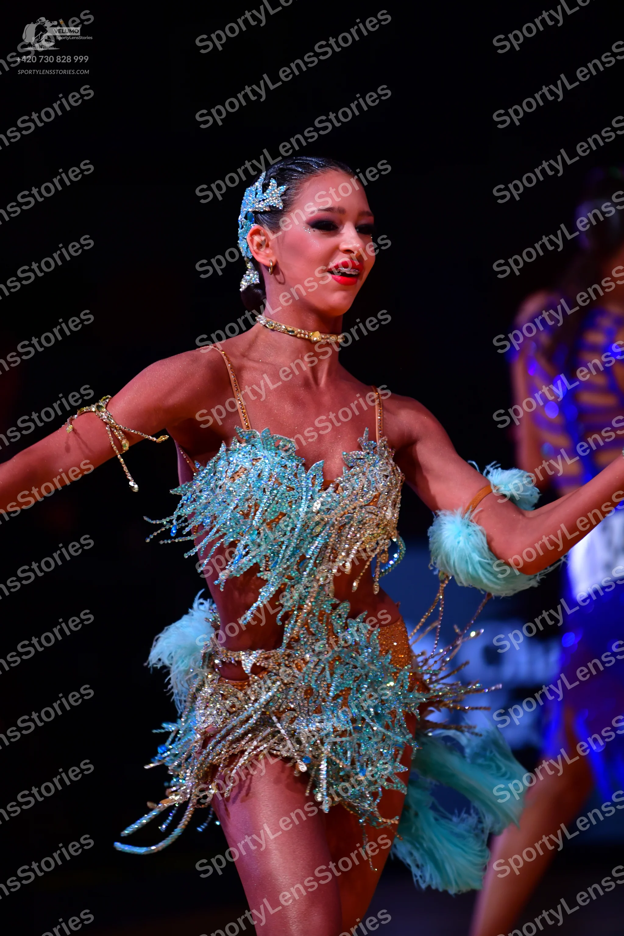 Dancesport competitor: Female dancer in foreground: light blue and gold Latin dance dress with heavy se