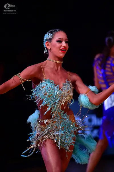 Dancesport competitor: Female dancer in foreground: light blue and gold Latin dance dress with heavy se