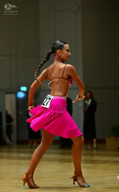 Dancesport competitor #27: Female dancer: bright pink latin dress with rhinestones, thin brown straps acros