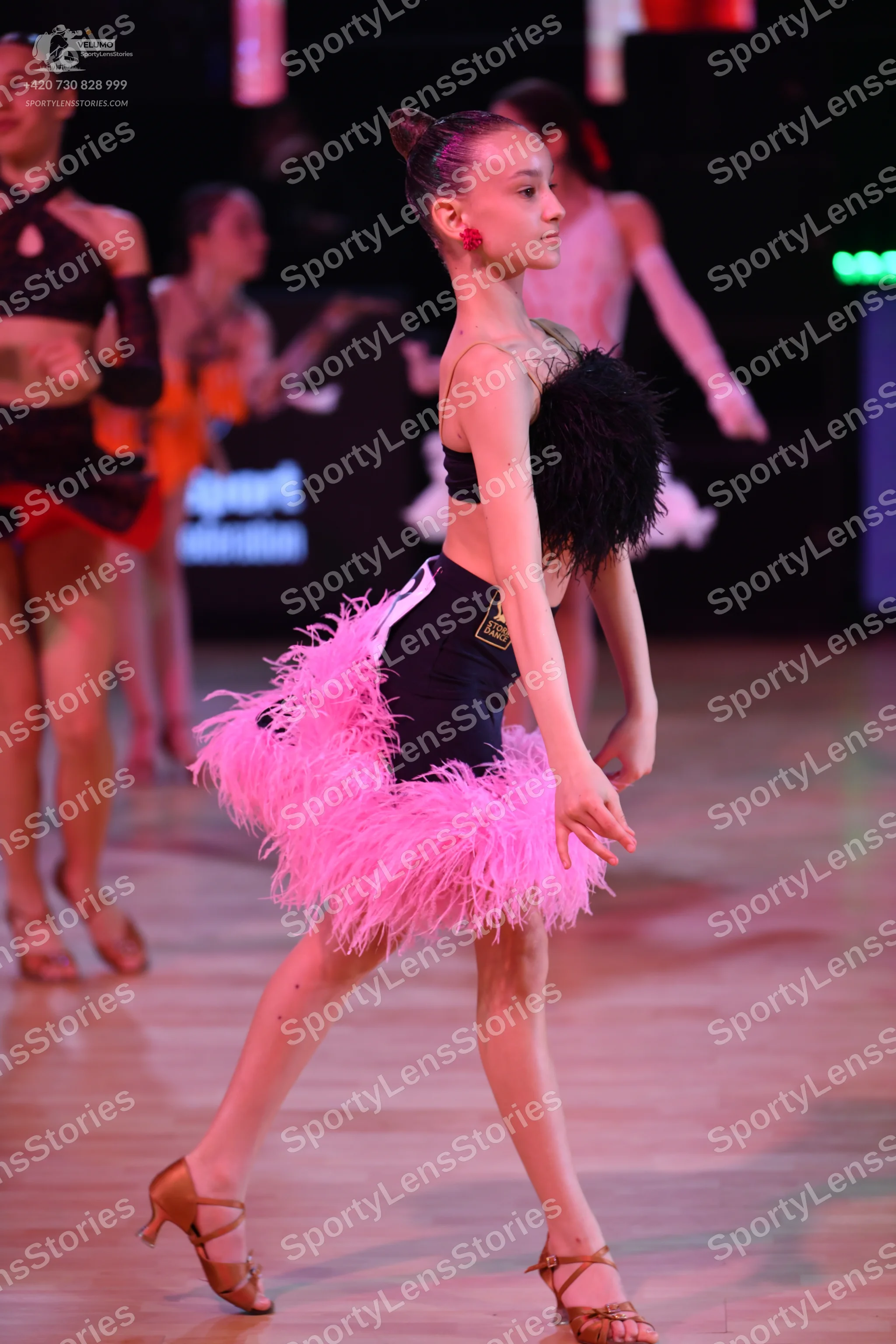 Dancesport competitor: Female dancer in foreground: black two-piece latin costume with pink feather ski