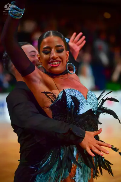 Dancesport competitor: Female dancer: light blue sequined Latin dress with large black feather accents,