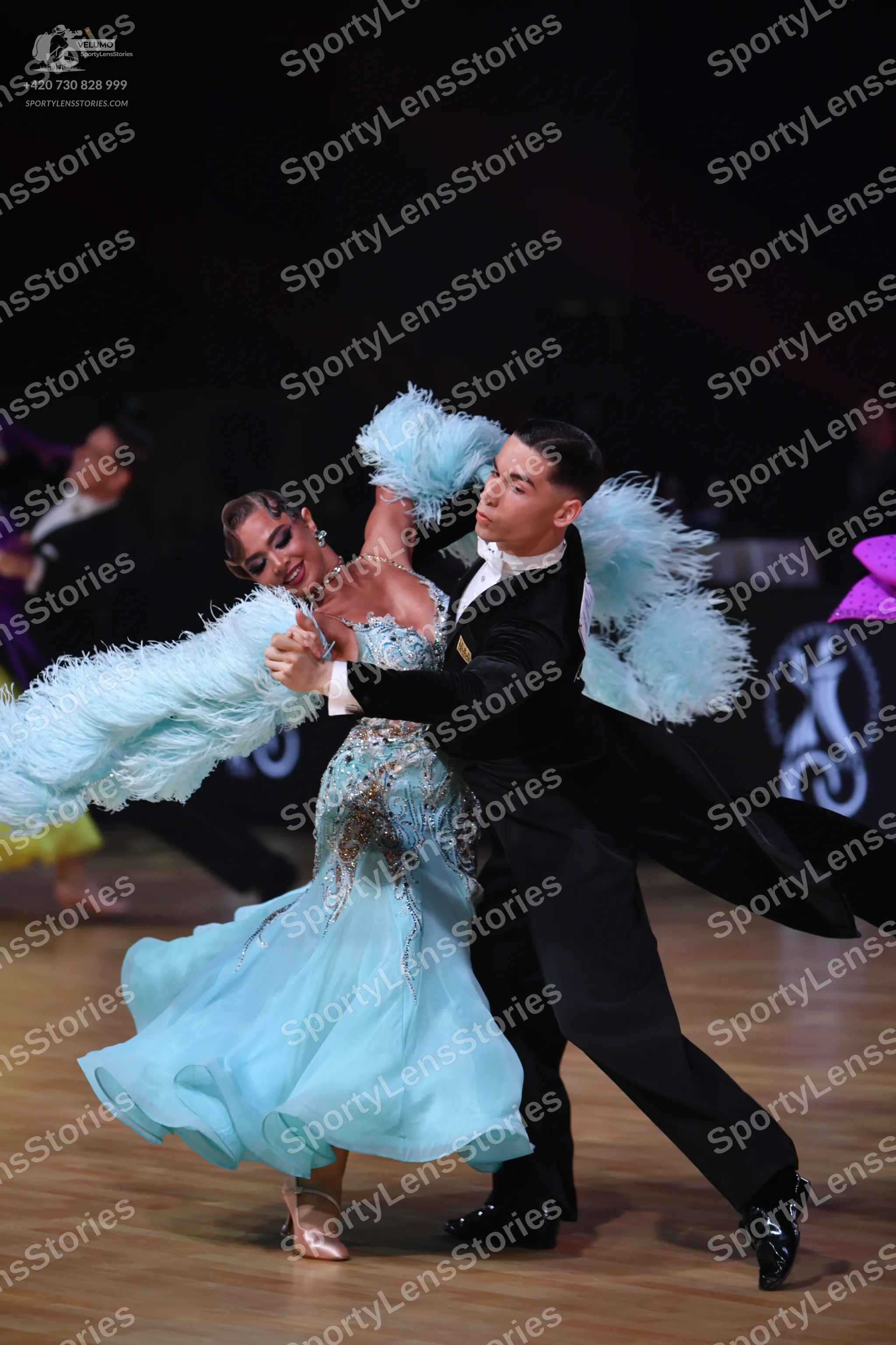 Dancesport competitor: Female dancer: light blue ballroom gown with large light blue feather trim on th