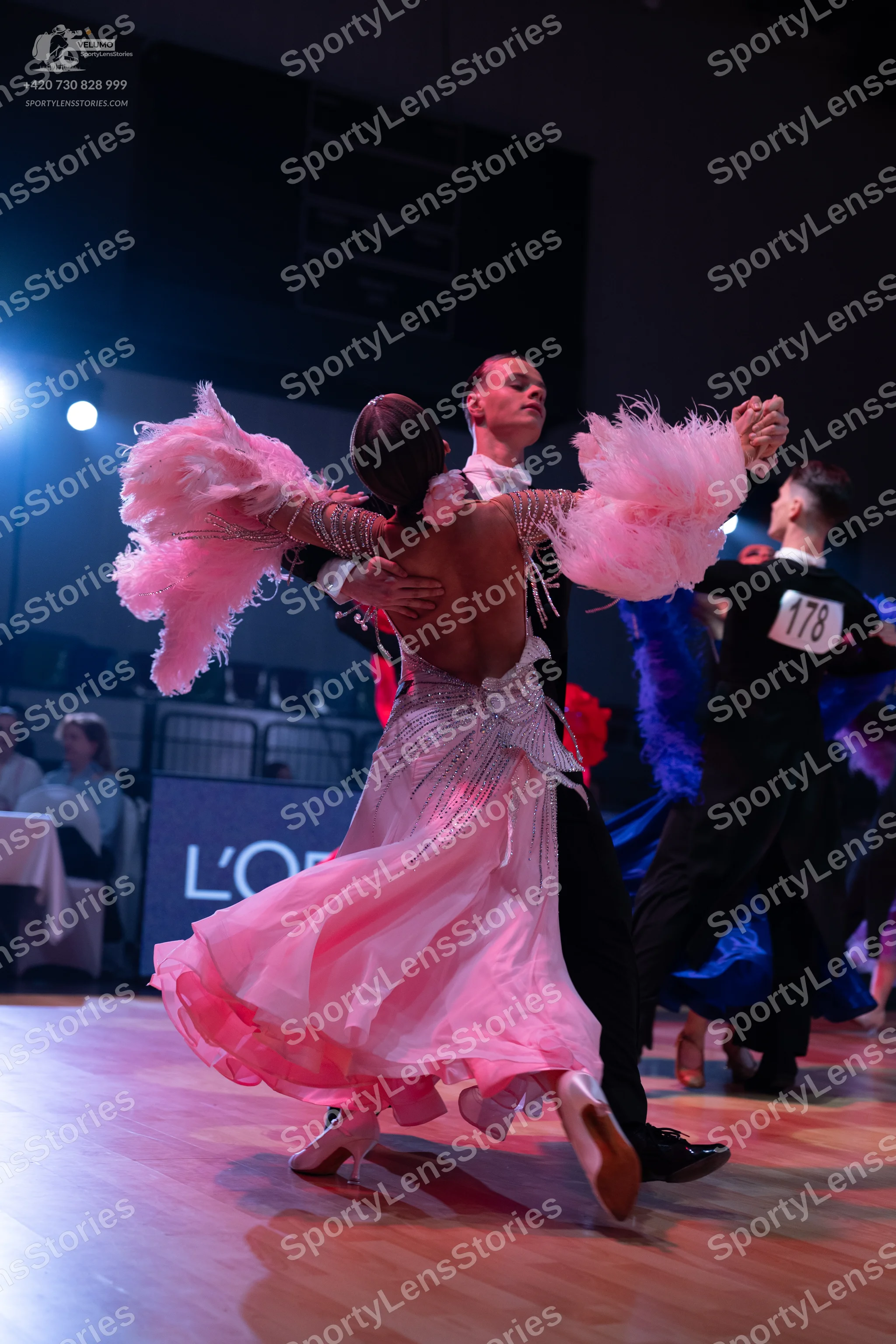 Dancesport competitor: Female dancer in foreground: light pink ballgown with voluminous pink feather-li