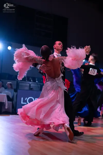 Dancesport competitor: Female dancer in foreground: light pink ballgown with voluminous pink feather-li