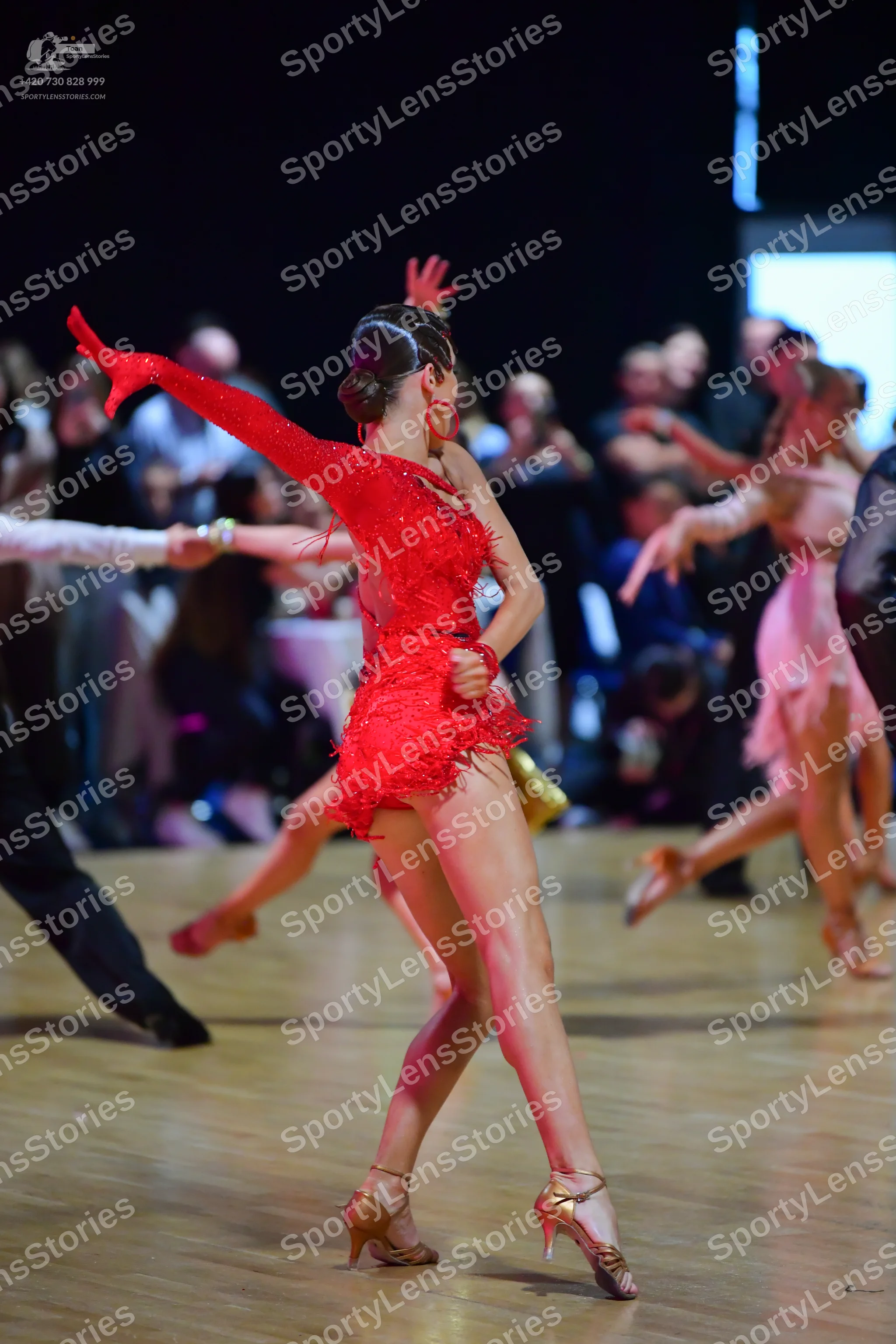 Dancesport competitor: Female dancer in foreground: red latin dress with long sleeves and fringe