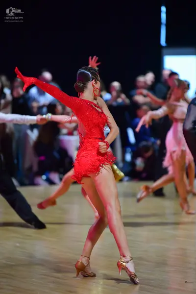 Dancesport competitor: Female dancer in foreground: red latin dress with long sleeves and fringe