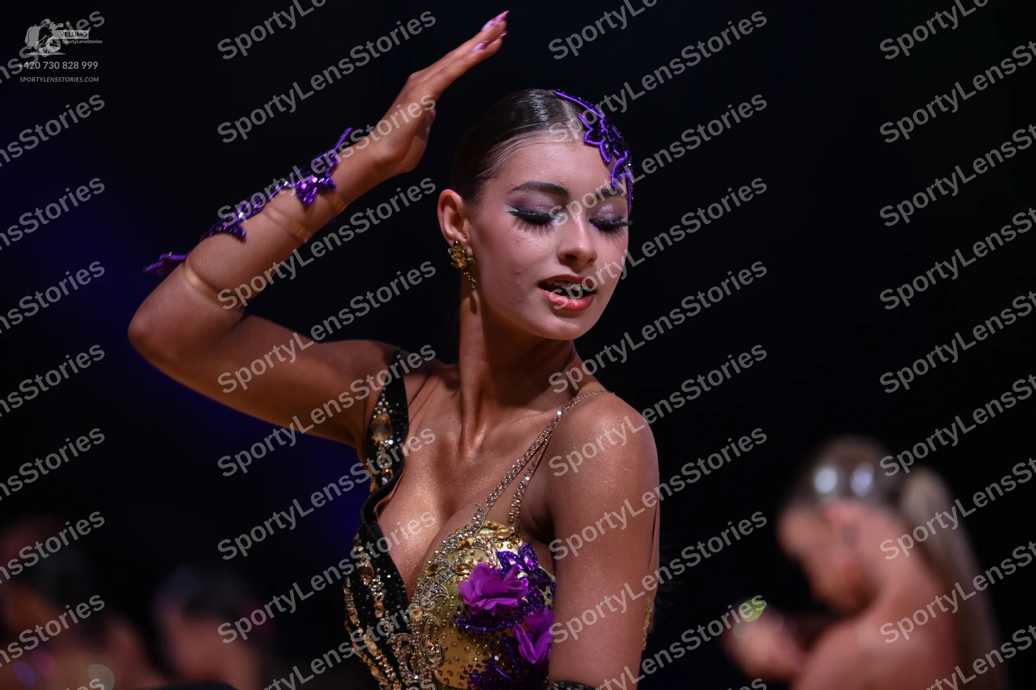 Dancesport competitor: Primary female dancer: gold and black Latin dance costume with purple floral seq