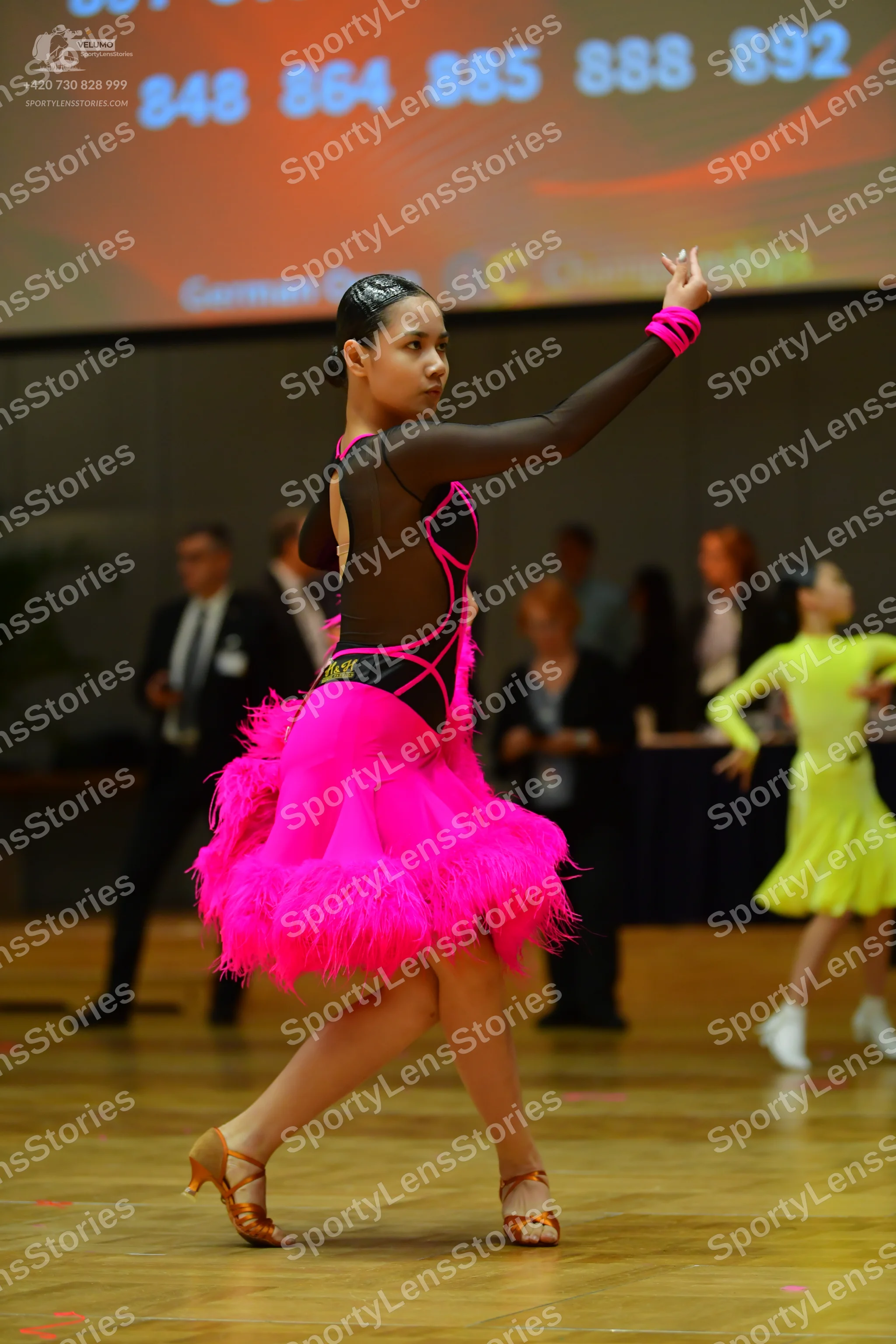 Dancesport competitor: Female dancer in foreground: black and pink Latin dance dress with a mesh bodice