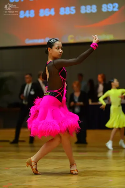 Dancesport competitor: Female dancer in foreground: black and pink Latin dance dress with a mesh bodice